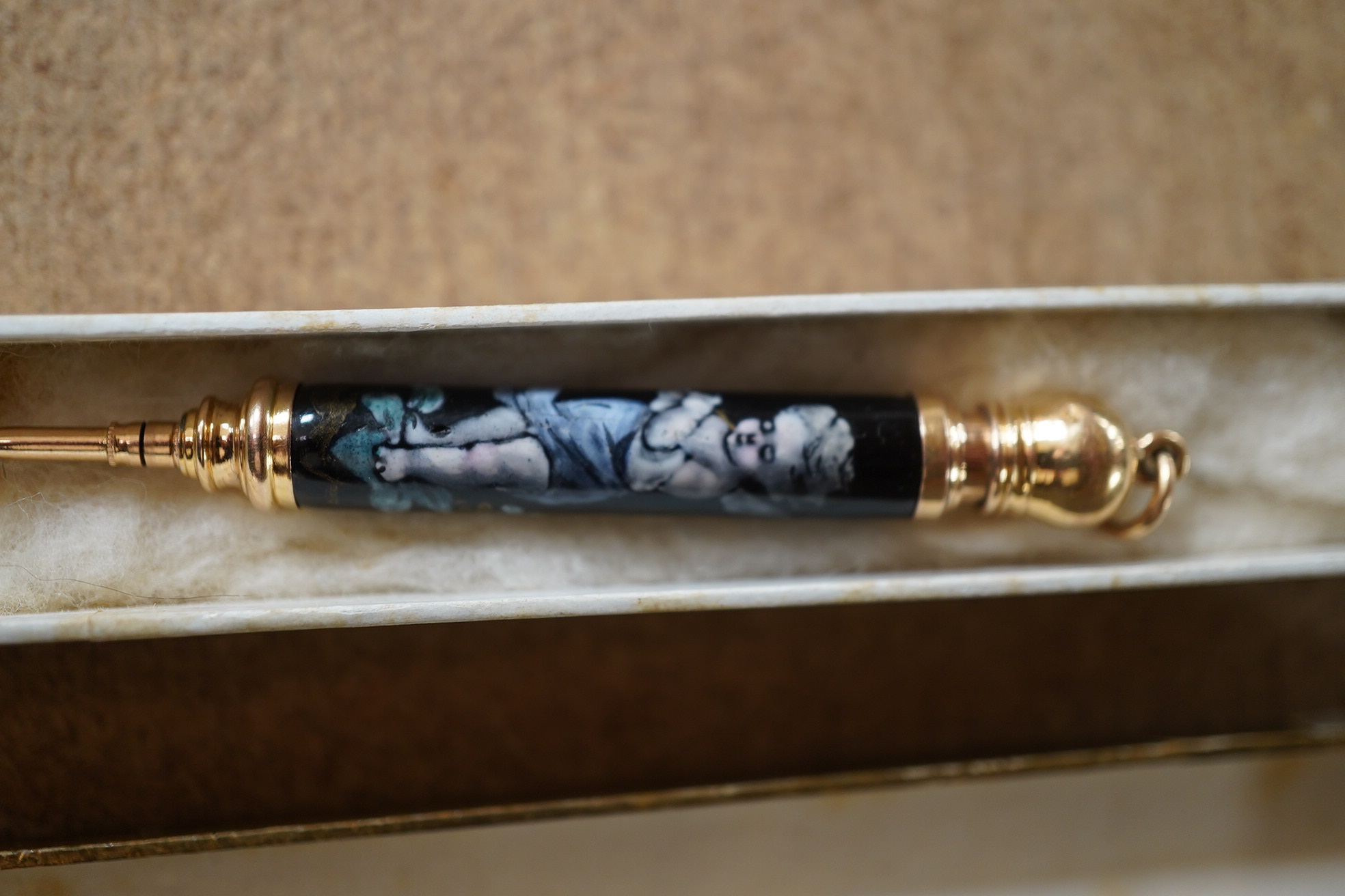 A Continental yellow metal and enamel propelling pencil decorated with putti, 72mm. Condition - poor (slight damage to the enamel).